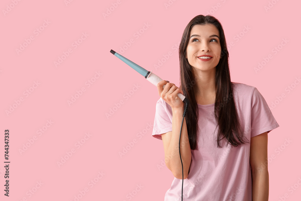 Beautiful young happy woman with curling iron on pink background Beautiful young happy woman with curling iron on pink background