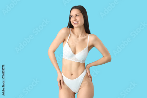 Slim young woman in white underwear on blue background