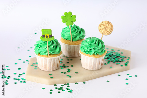 Fototapeta Naklejka Na Ścianę i Meble -  Stand with tasty cupcakes and sequins for St. Patrick's Day on white background