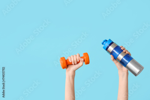 Female hands with dumbbell and bottle of water on color background