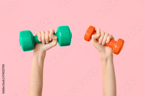 Female hands with colorful dumbbells on pink background, closeup