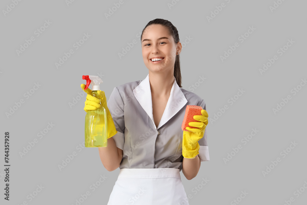 Young chambermaid with cleaning sponge and detergent on light background