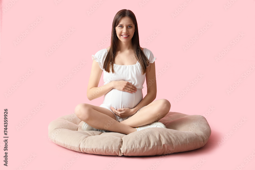 Young pregnant woman sitting on pouf against pink background Young pregnant woman sitting on pouf against pink background