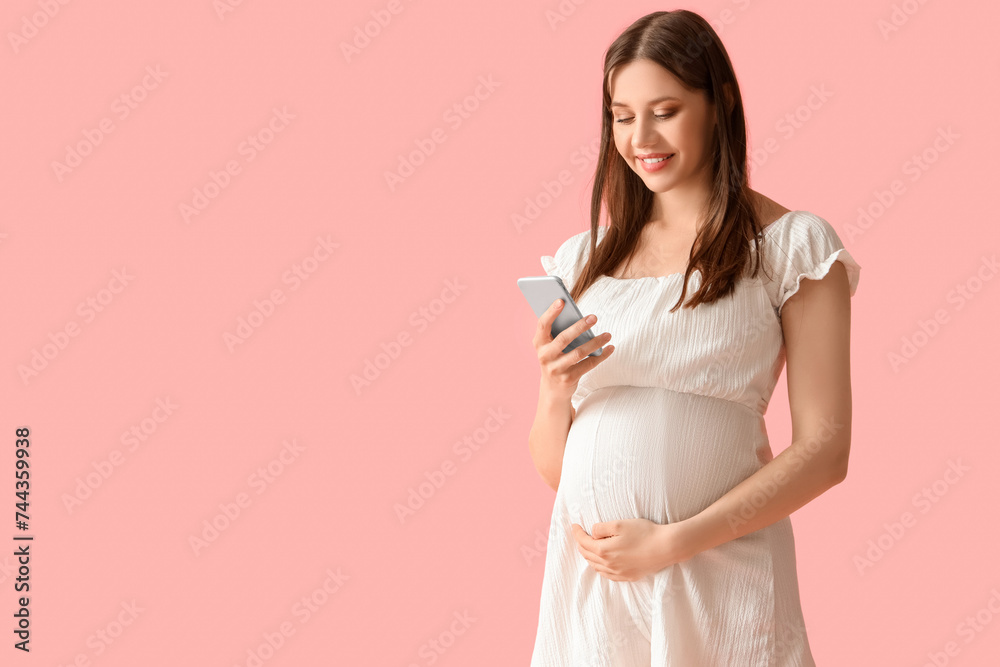 Young pregnant woman using mobile phone on pink background Young pregnant woman using mobile phone on pink background