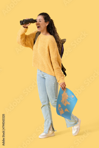 Female African-American traveler with world map looking through binoculars on yellow background