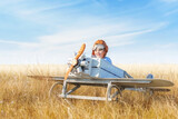 Little boy is playing the plane. Happy and funy child imagines himself an aircraft pilot and plays in a aviator costume in an open-air field against a blue sky on a summer sunny day. 
