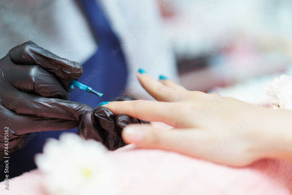 Painting a glossy color on woman finger nails close up.