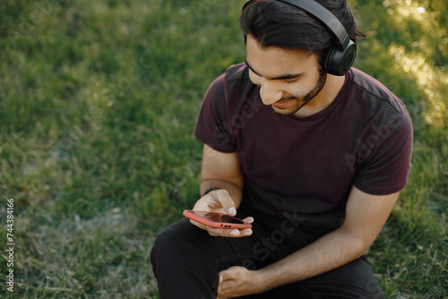 Male indian student sitting on a grass and using a smatphone