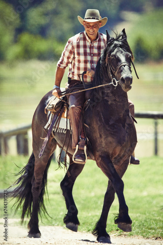 Cowboy, smile and man riding horse with saddle on field in countryside for equestrian or training. Agriculture, summer and happy mature horseback rider on animal at ranch outdoor in rural Texas