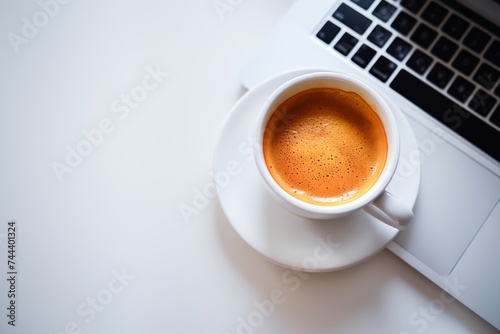 A simple and clean image of a cup of coffee next to a laptop on a white desk, perfect for concepts related to work and productivity.