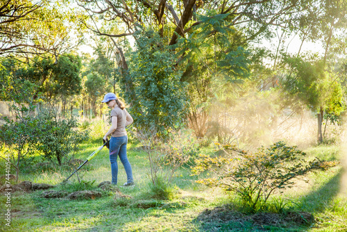 Teen girl cutting grass with whipper snipper in golden afternoon light photo