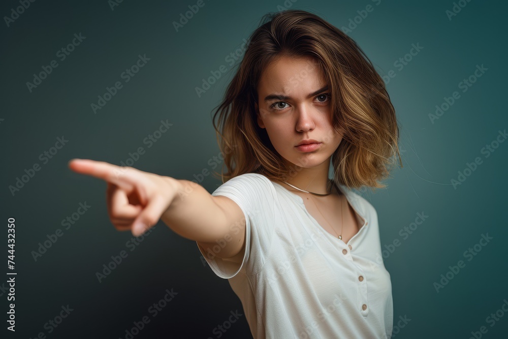 A young woman with a serious expression pointing directly at the camera with a blurred background. A young woman with a serious expression pointing directly at the camera with a blurred background.