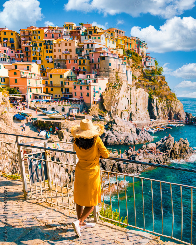 Asian women visiting Manarola in Cinque Terre Italy,beautiful colorful town of La Spezia Liguria one of the five Cinque Terre, woman with hat standing by the ocean during summer in Europe