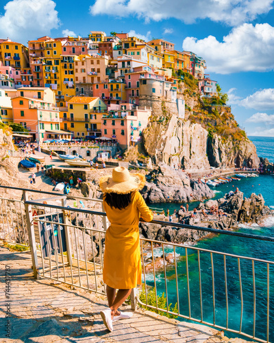 Asian women visiting Manarola in Cinque Terre Italy,beautiful colorful town of La Spezia Liguria one of the five Cinque Terre, woman with hat standing by the ocean during summer in Europe
