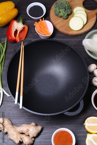 Empty iron wok, chopsticks and ingredients on dark grey wooden table, above view