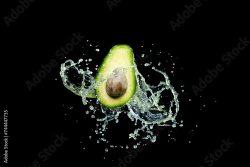 Half an avocado on a black background in splashes of water.