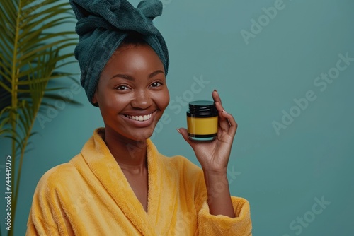A cheerful African woman in a bathrobe is seen applying cream to her face
