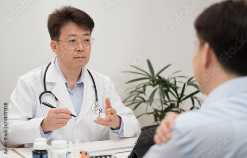 A middle-aged Asian male doctor and a male patient undergoing counseling at a hospital