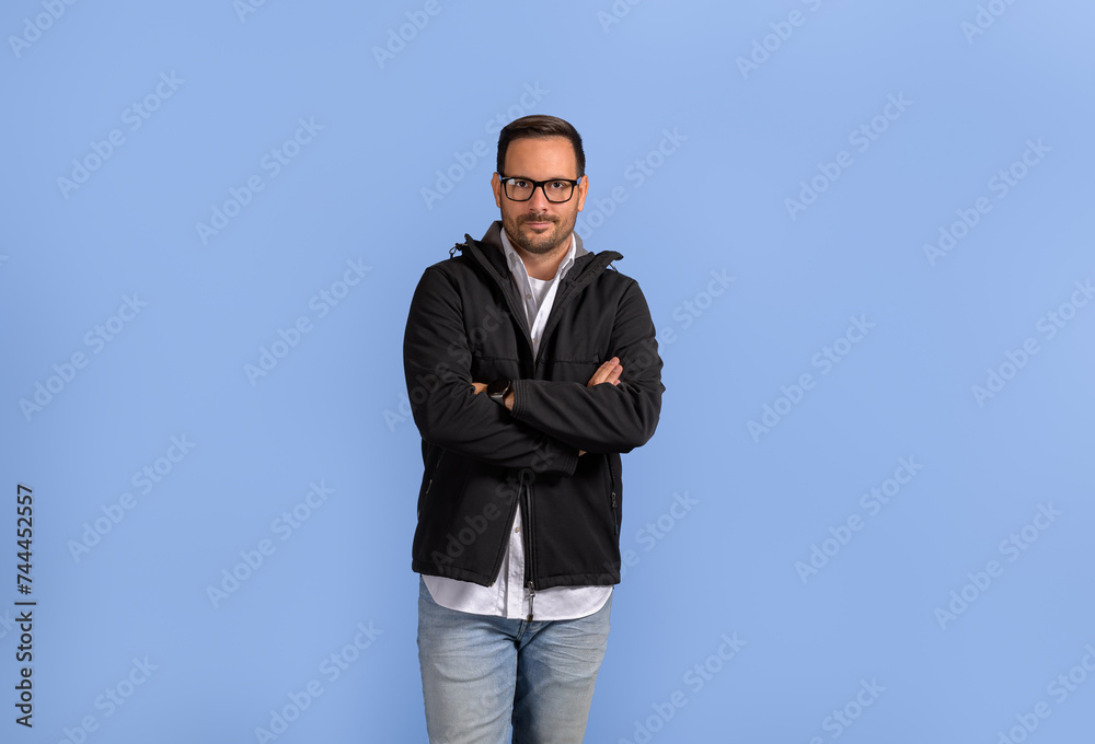 Portrait of confident male entrepreneur in eyeglasses standing with arms crossed on blue background Portrait of confident male entrepreneur in eyeglasses standing with arms crossed on blue background