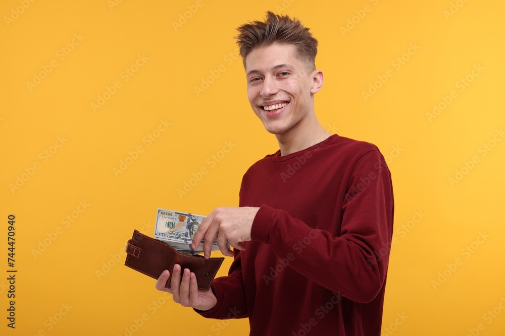 Happy man putting money into wallet on yellow background Happy man putting money into wallet on yellow background