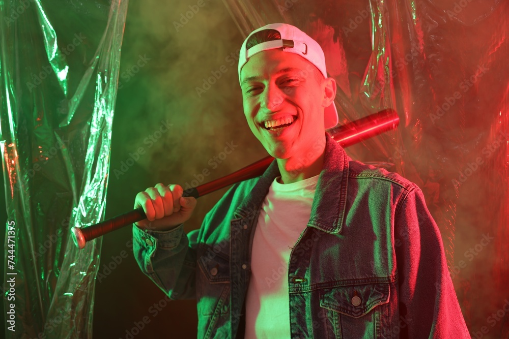 Fototapeta premium Young man with baseball bat on color background in neon lights