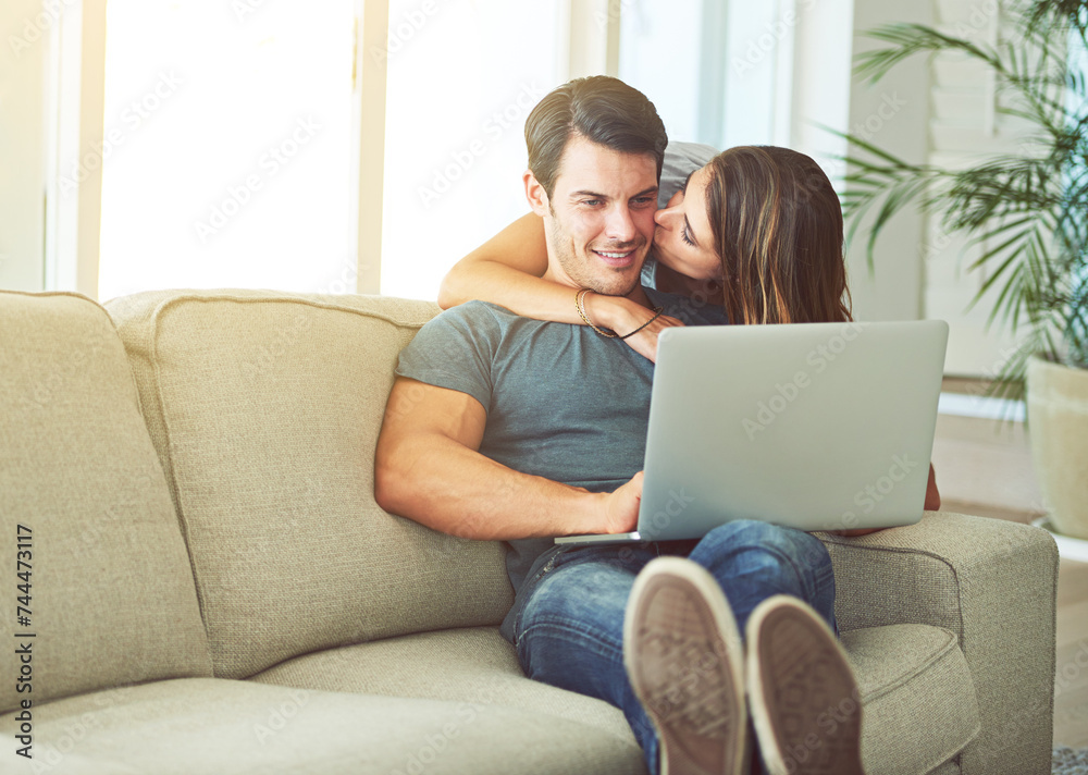 Laptop, kiss and woman hugging man on sofa networking on social media, website or internet. Happy, love and female person embracing husband reading online blog with computer in living room at home. Laptop, kiss and woman hugging man on sofa networking on social media, website or internet. Happy, love and female person embracing husband reading online blog with computer in living room at home.
