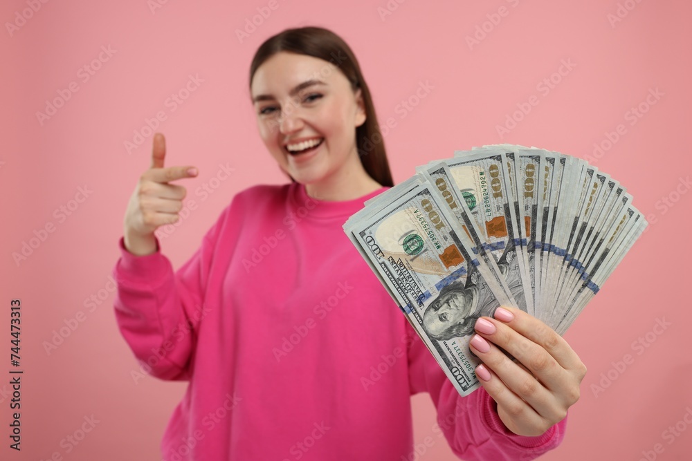 Happy woman pointing at dollar banknotes on pink background, selective focus Happy woman pointing at dollar banknotes on pink background, selective focus