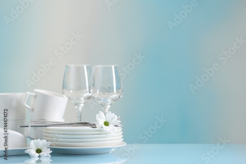 Set of many clean dishware, cutlery, flowers and glasses on light blue table. Space for text photo