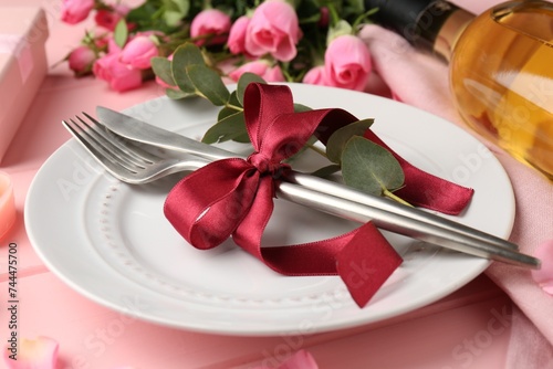 Romantic place setting. Plate, cutlery, eucalyptus branch and roses on pink table, closeup