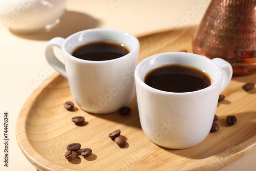 Delicious coffee in cups and beans on beige table, closeup