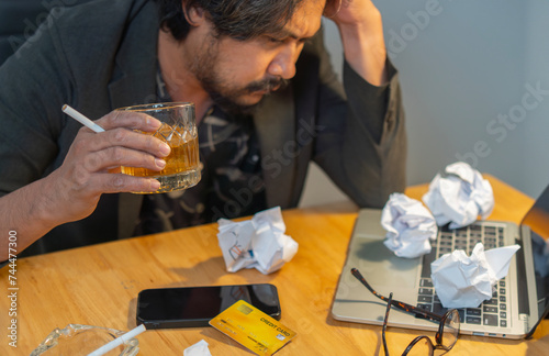 Bearded male hold head with hands look down sitting at office feels depressed desperate  drinking strong alcoholic