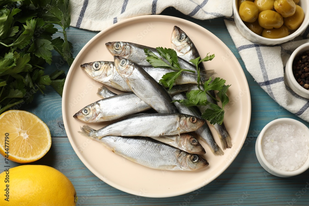 Fresh raw sprats, parsley and other products on light blue wooden table, flat lay - obrazy, fototapety, plakaty 