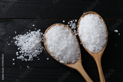Organic salt in spoons on black wooden table, top view