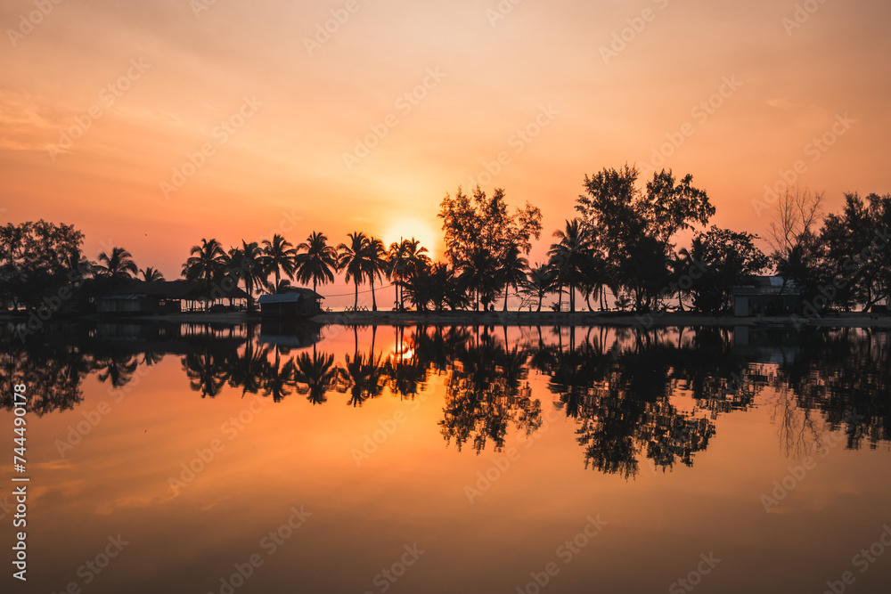 A sunset view of a tropical beach silhouetted against the orange sky