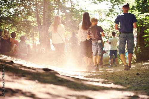 Festival, party and family walking in forest outdoor together for event, celebration or social gathering. Mother, father and children in nature, park or woods for summer entertainment from back photo