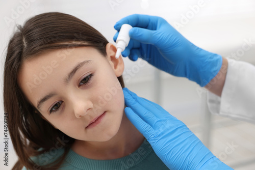 Doctor applying medical drops into girl's ear indoors