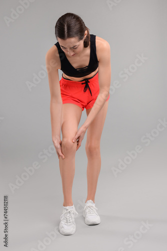 Young woman suffering from leg pain on grey background
