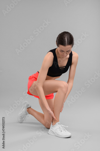 Young woman suffering from leg pain on grey background