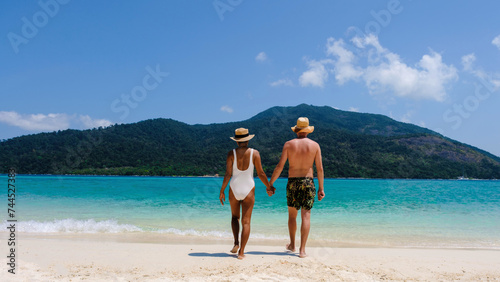 rear view of a Couple on the beach Koh Lipe Island Thailand, tropical Island with a blue ocean and white soft sand. men and women relaxing on the beach walking to the blue ocean, bikini and swim short