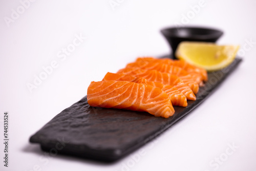 Freshly sliced salmon fillet isolated on a black stone plate with soy sauce and lemon wedge