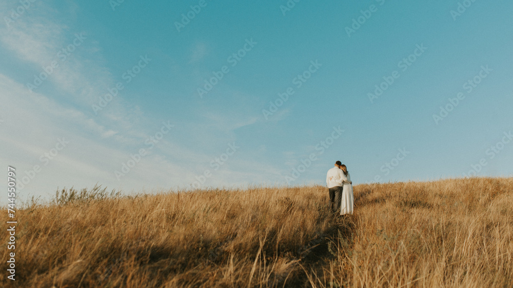 Couple standing on the top of the hill in the wheat meadow. Beautiful landscape of deep blue sky and wheat field. Couple hugs in the middle of nature. couple outdoors enjoying the fresh air

