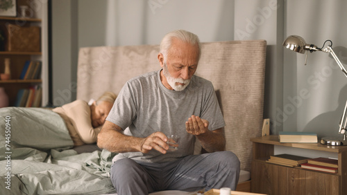 Elderly man taking medication with water in bedroom