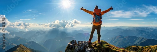 A mountain climber at the mountain top raises his hands. He is overlooking a stunning landscape. © Simon