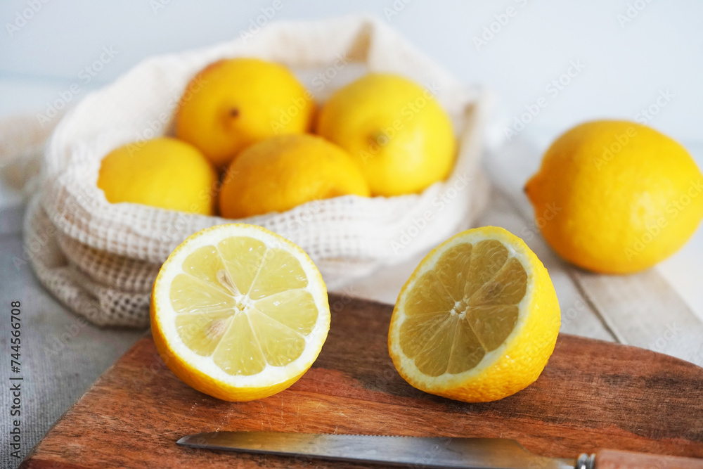 Whole lemons next to cut ones on a wooden board next to a knife on a light background Whole lemons next to cut ones on a wooden board next to a knife on a light background