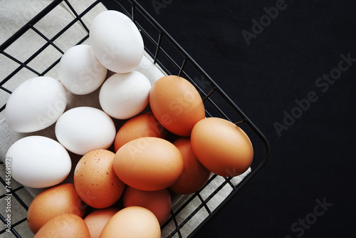 Brown and white chicken eggs in a metal basket on a dark light background