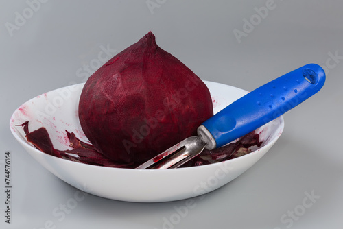 Raw peeled red beetroot and peeler among peelings in bowl