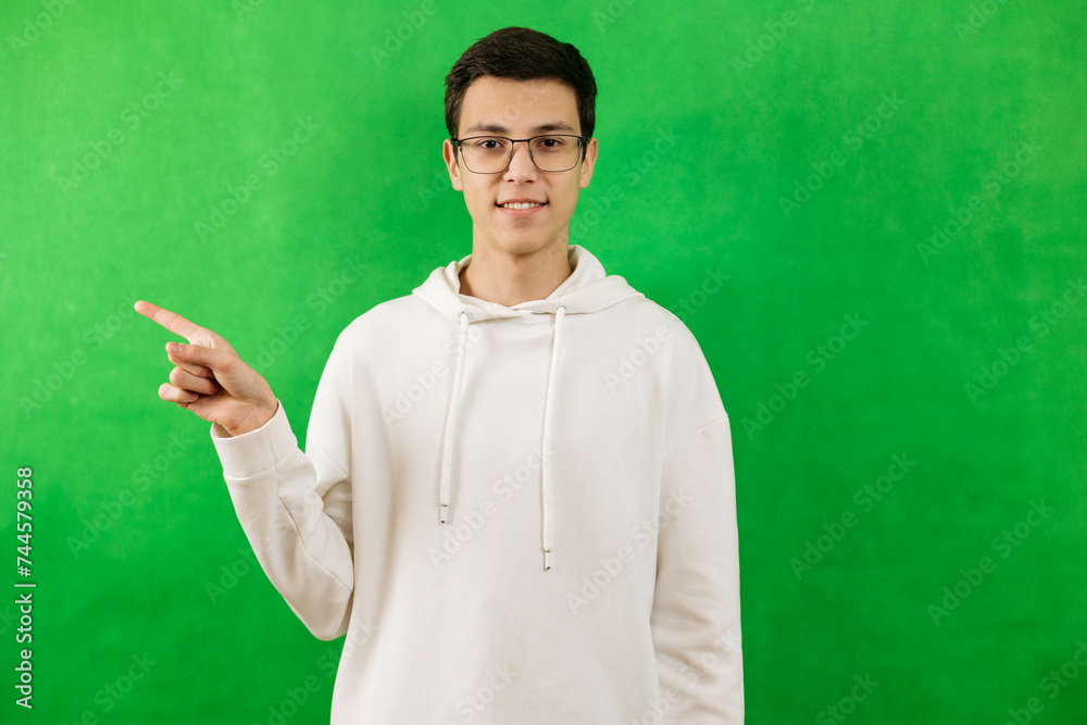 Portrait of a young man on a green background, wearing glasses, pointing his finger to the side. Copy space Portrait of a young man on a green background, wearing glasses, pointing his finger to the side. Copy space