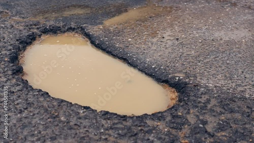 A large pothole in the middle of a crumbling road in the countryside. Close-up of a hole on the road during the rain. photo