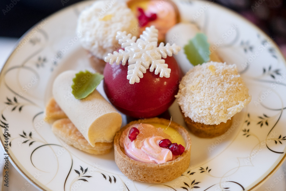 Assortment of bite-sized cakes such as fruit tartlets, cheesecakes, coconut marshmallow balls and a red chocolate sphere decorated with a sugar snowflake, elegant dessert served with teas or coffees Assortment of bite-sized cakes such as fruit tartlets, cheesecakes, coconut marshmallow balls and a red chocolate sphere decorated with a sugar snowflake, elegant dessert served with teas or coffees