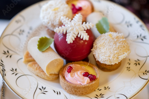 Assortment of bite-sized cakes such as fruit tartlets, cheesecakes, coconut marshmallow balls and a red chocolate sphere decorated with a sugar snowflake, elegant dessert served with teas or coffees